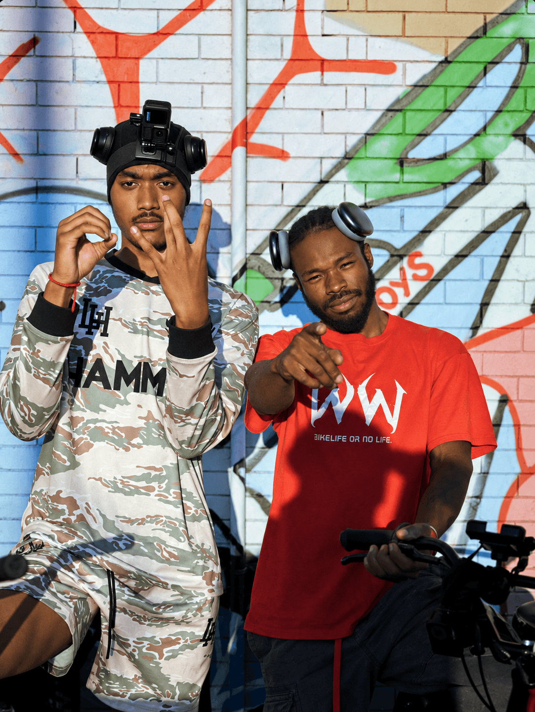 Two riders in front of a painted brick wall
